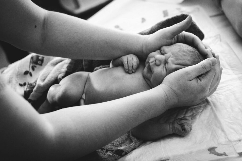 Neugeborenes wird von Hebamme untersucht - Geburtsfotografie Kärnten